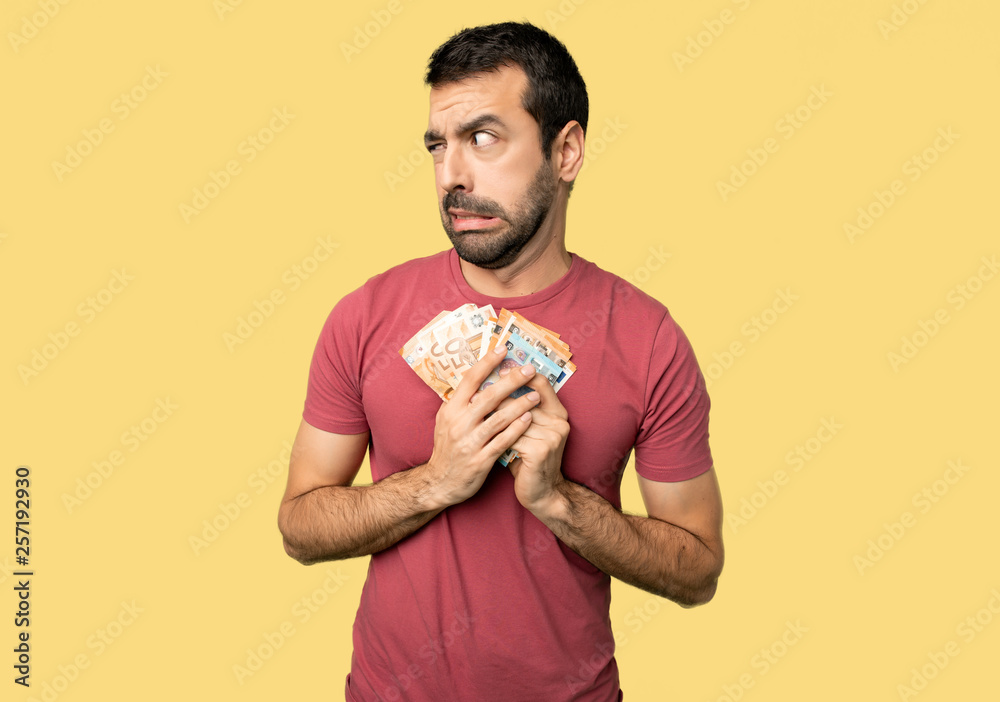 Man taking a lot of money is a little bit nervous and scared pressing the teeth on isolated yellow background Man taking a lot of money is a little bit nervous and scared pressing the teeth on isolated yellow background