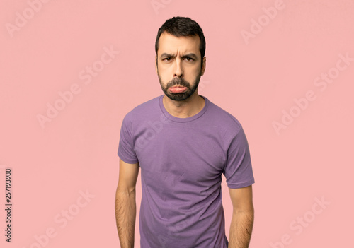 Handsome man with sad and depressed expression on isolated pink background