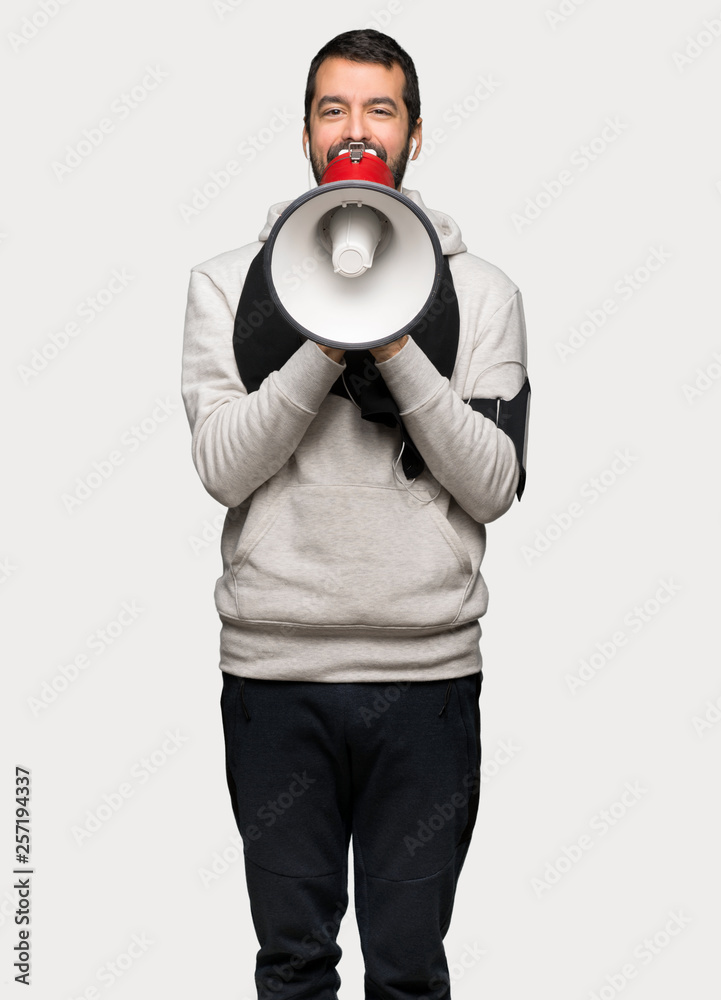 Sport man shouting through a megaphone to announce something over isolated grey background Sport man shouting through a megaphone to announce something over isolated grey background