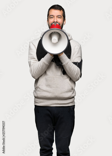Sport man shouting through a megaphone to announce something over isolated grey background