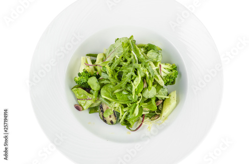 Salad of green vegetables with broccoli, zucchini and walnut dressing on a plate on a white background, top view isolated
