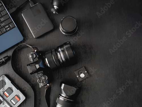 top view of work space photographer with digital camera, flash, cleaning kit, memory card, external harddisk, USB card reader, laptop and camera accessory on black table background. photo