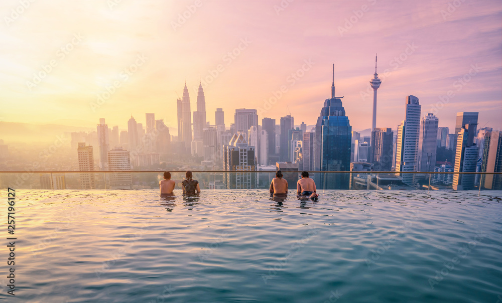 Naklejka premium Podróżujący patrząc na panoramę miasta Kuala Lumpur w basenie na dachu hotelu o wschodzie słońca w Kuala Lumpur, Malezja.