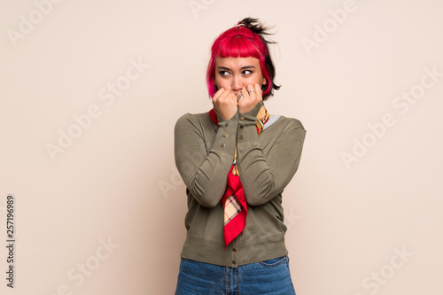 Young woman with pink hair over yellow wall nervous and scared putting hands to mouth