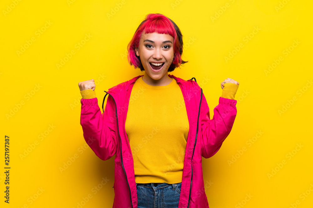 Fototapeta premium Young woman with pink hair over yellow wall celebrating a victory in winner position