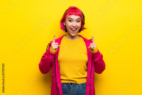 Young woman with pink hair over yellow wall pointing up a great idea