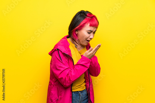 Young woman with pink hair over yellow wall is suffering with cough and feeling bad