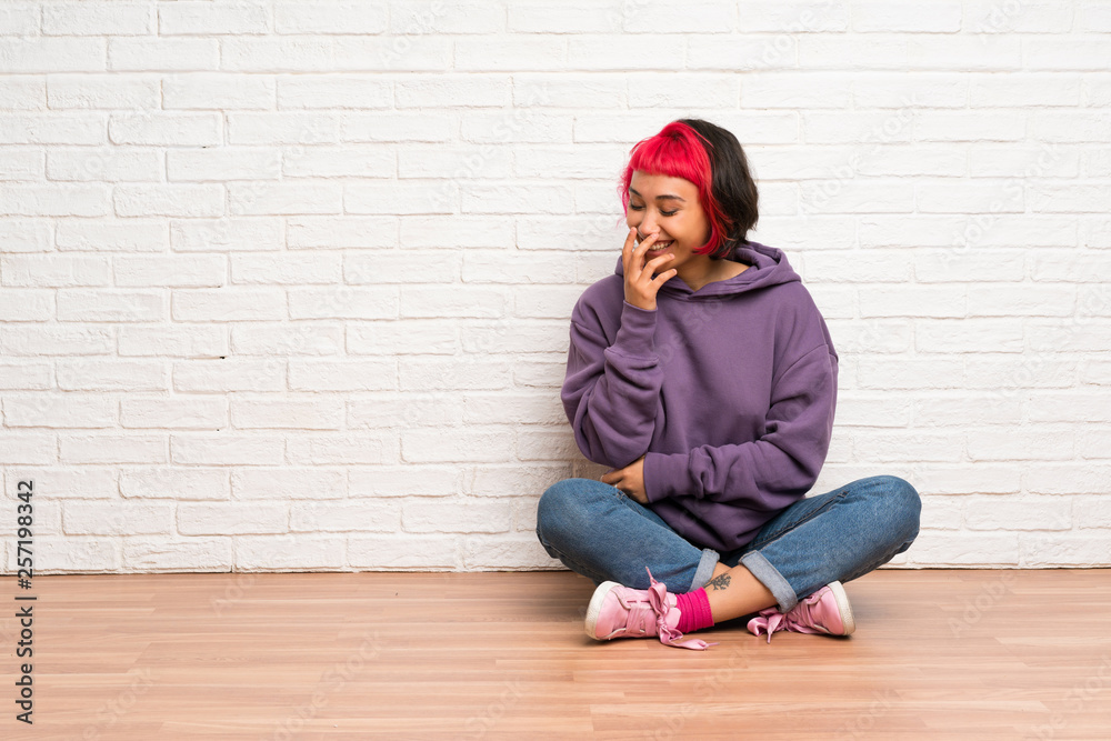 Young woman with pink hair sitting on the floor smiling a lot Young woman with pink hair sitting on the floor smiling a lot