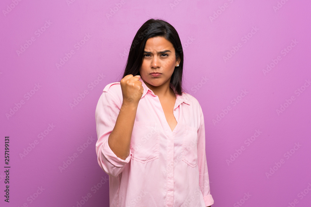 Young Colombian girl over purple wall with angry gesture
