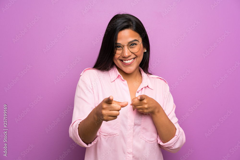 Young Colombian girl over purple wall points finger at you Young Colombian girl over purple wall points finger at you