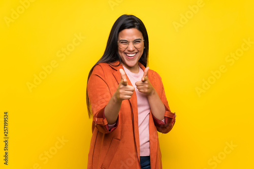 Young Colombian girl over yellow wall pointing to the front and smiling © luismolinero