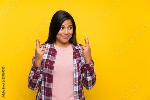 Young Colombian girl over yellow wall with fingers crossing