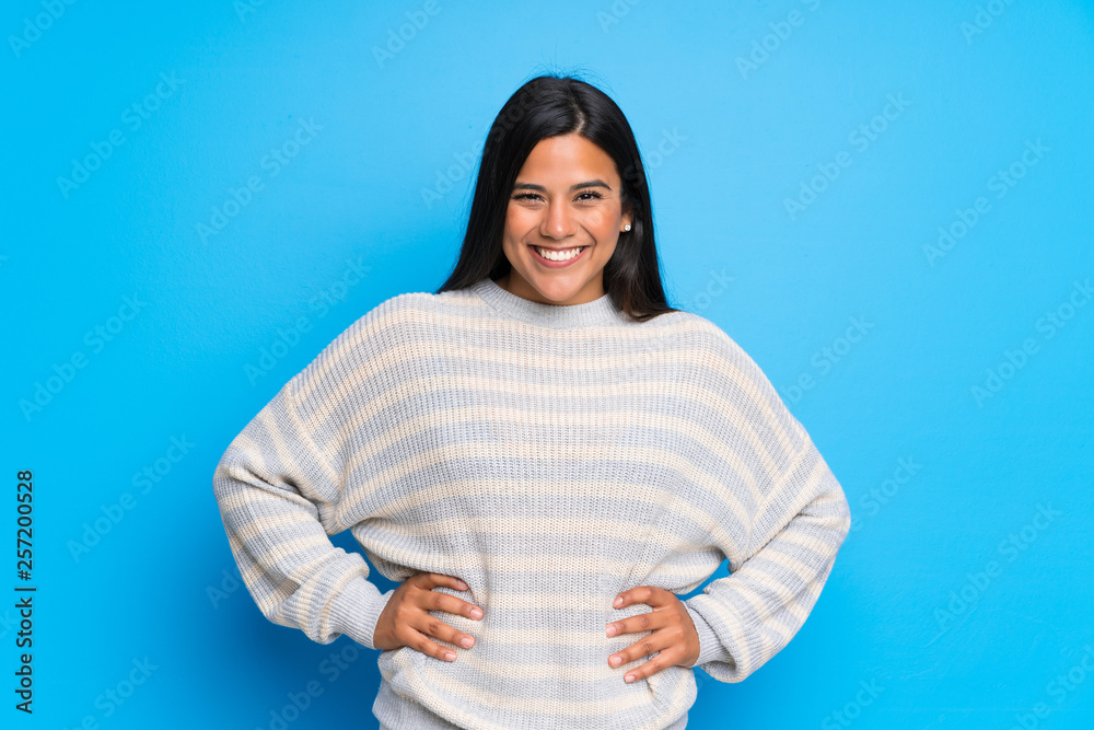 Young Colombian girl with sweater posing with arms at hip and laughing looking to the front Young Colombian girl with sweater posing with arms at hip and laughing looking to the front
