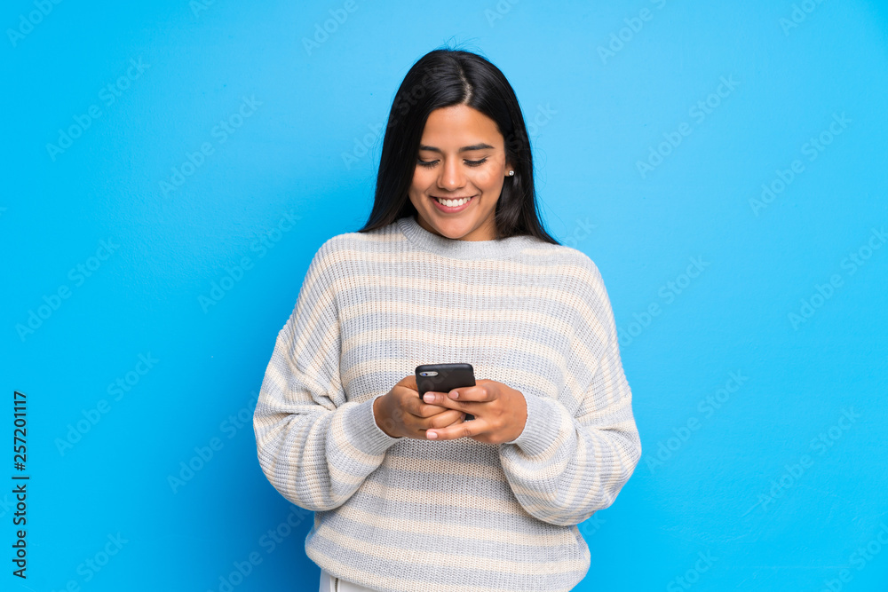 Young Colombian girl with sweater sending a message with the mobile Young Colombian girl with sweater sending a message with the mobile