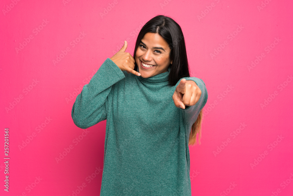 Young Colombian girl with green sweater making phone gesture and pointing front