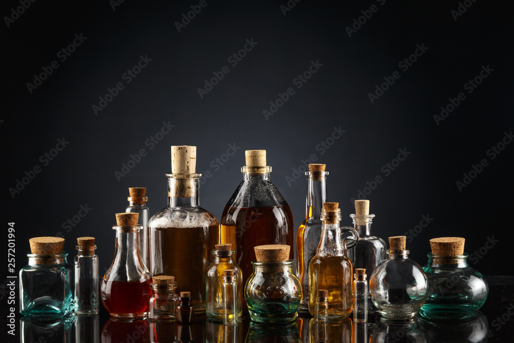 Glass bottles of different shapes and sizes filled with liquids of different colors on a black background. Glass bottles of different shapes and sizes filled with liquids of different colors on a black background.