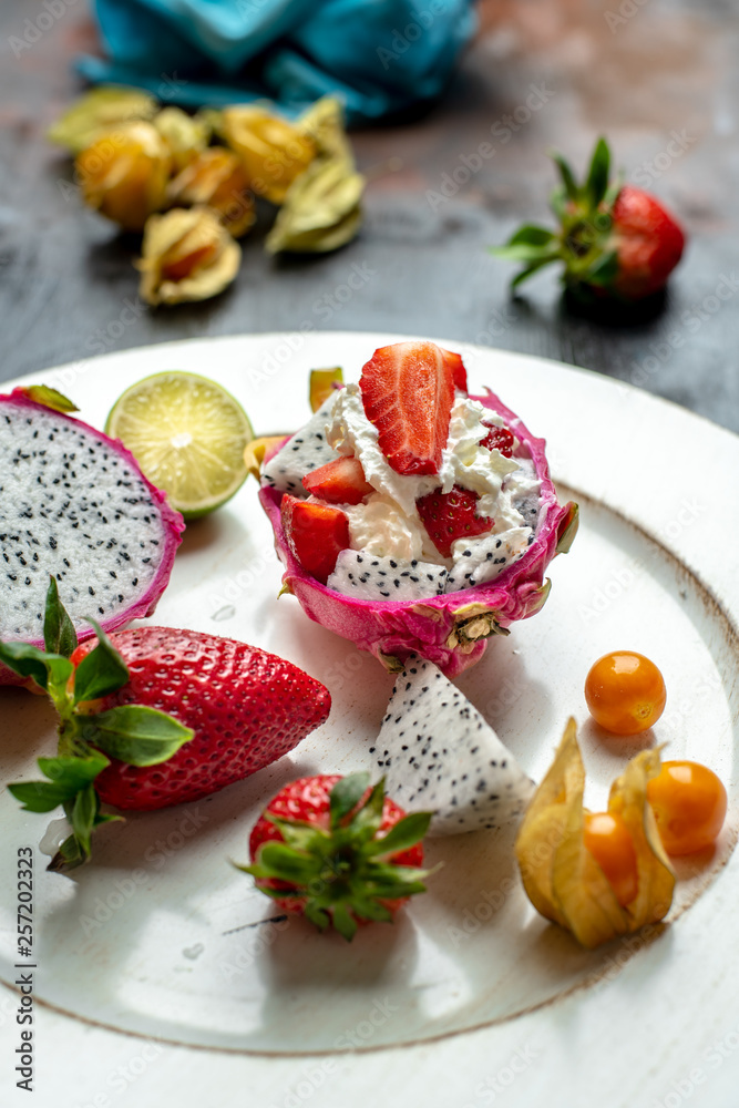 on a white, wooden plate, lie the fresh fruit of strawberries, among them a beautiful, pink dragon fruit filled with whipped cream and strawberries on a white, wooden plate, lie the fresh fruit of strawberries, among them a beautiful, pink dragon fruit filled with whipped cream and strawberries