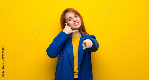 Cuadro en lienzo Young redhead woman with trench coat making phone gesture and pointing front