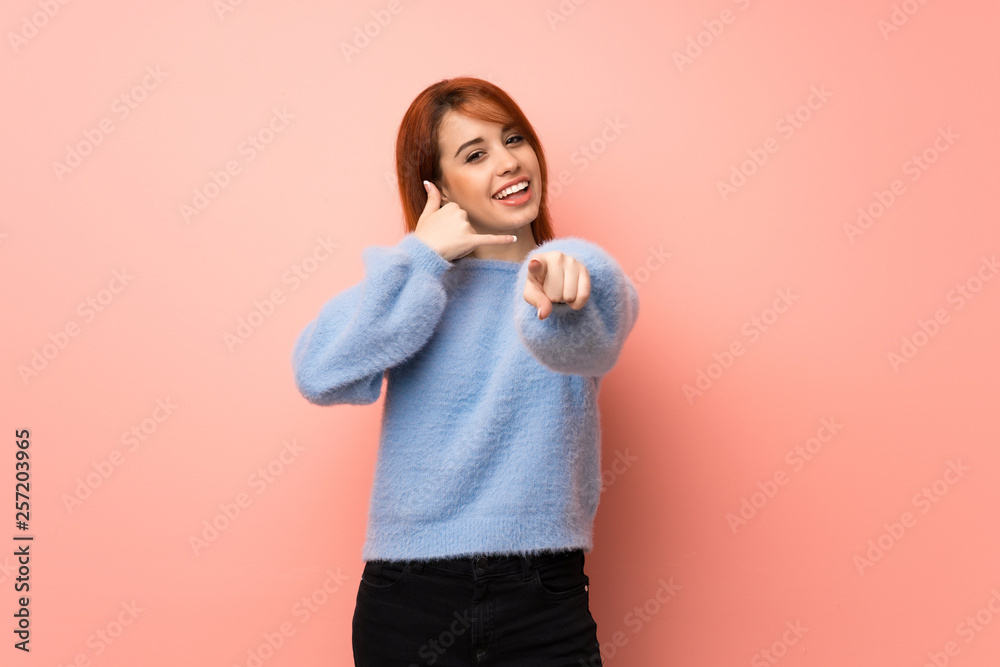 Young redhead woman over pink background making phone gesture and pointing front Young redhead woman over pink background making phone gesture and pointing front