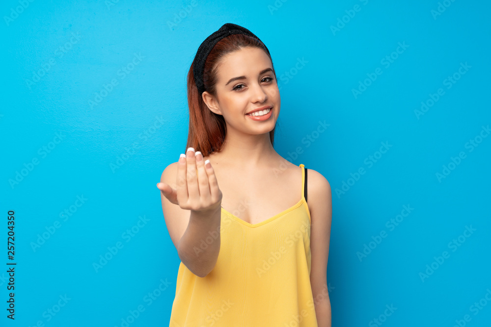 Fototapeta premium Young redhead woman over blue background inviting to come with hand. Happy that you came