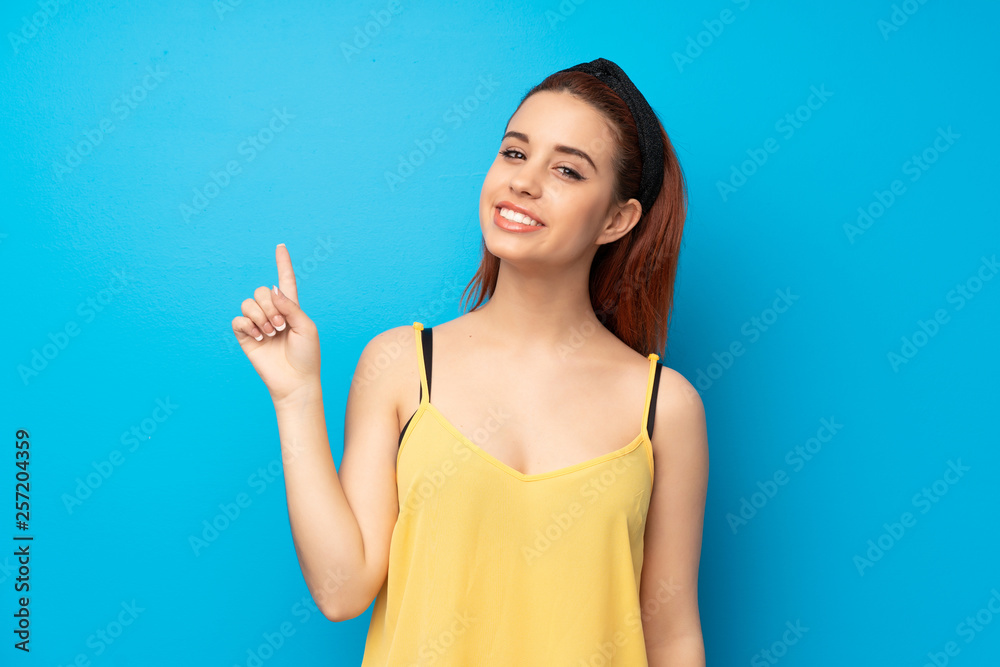 Young redhead woman over blue background showing and lifting a finger in sign of the best Young redhead woman over blue background showing and lifting a finger in sign of the best