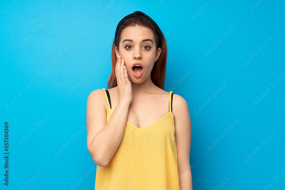 Young redhead woman over blue background with surprise and shocked facial expression Young redhead woman over blue background with surprise and shocked facial expression