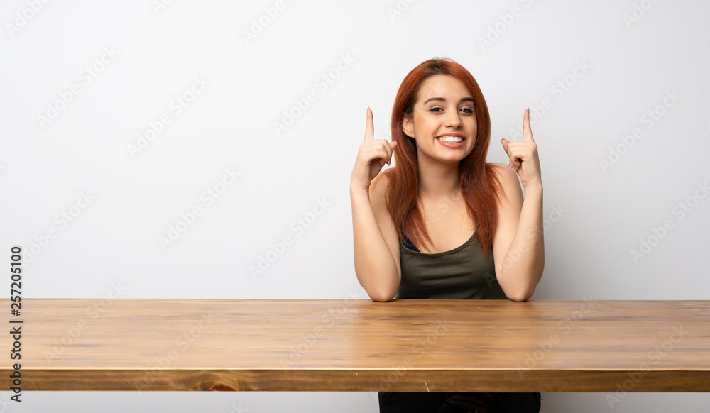 Young redhead woman at desk pointing with the index finger a great idea Young redhead woman at desk pointing with the index finger a great idea