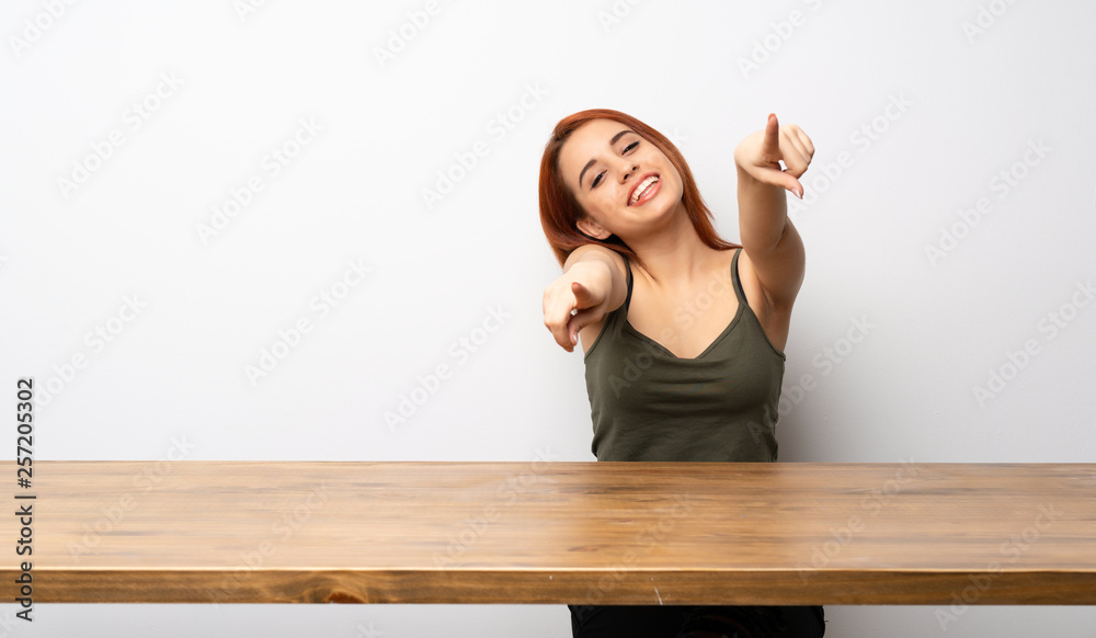 Young redhead woman at desk points finger at you while smiling Young redhead woman at desk points finger at you while smiling