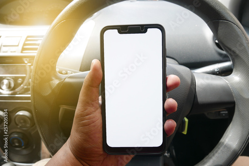 Close up of hand holding phone with white screen inside a car. Smartphone with mockup on background of car dashboard.