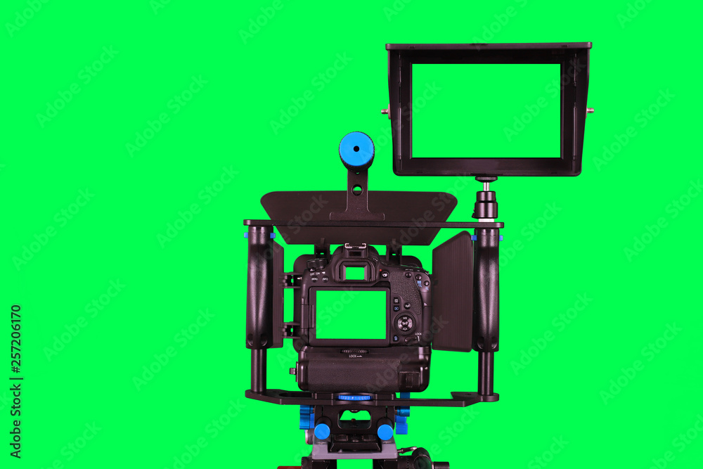 Fototapeta premium Dslr camera with additional screen for video shooting with green screen on the tripod isolated on green background. The chromakey. Green screen.
