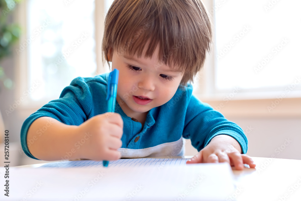 Toddler boy drawing with pen and paper at his desk Toddler boy drawing with pen and paper at his desk