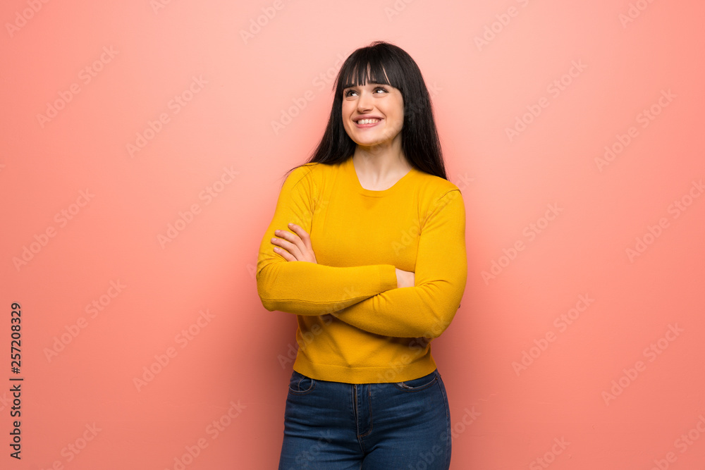Woman with yellow sweater over pink wall looking up while smiling Woman with yellow sweater over pink wall looking up while smiling