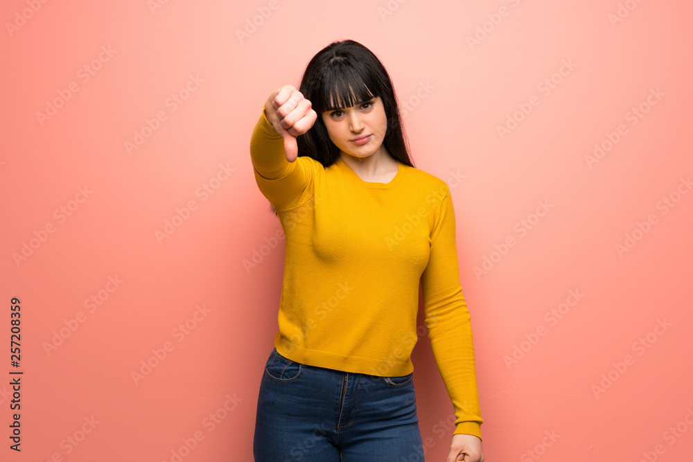 Woman with yellow sweater over pink wall showing thumb down with negative expression Woman with yellow sweater over pink wall showing thumb down with negative expression