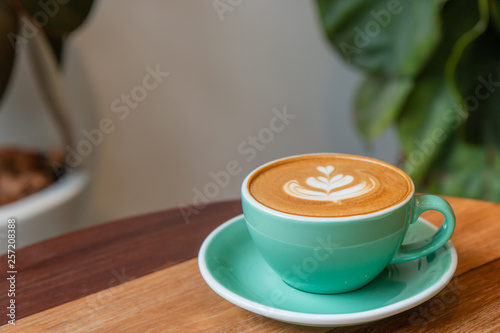 Hot cappuccino coffee in a green cup with latte art on the wooden table in the coffee shop.