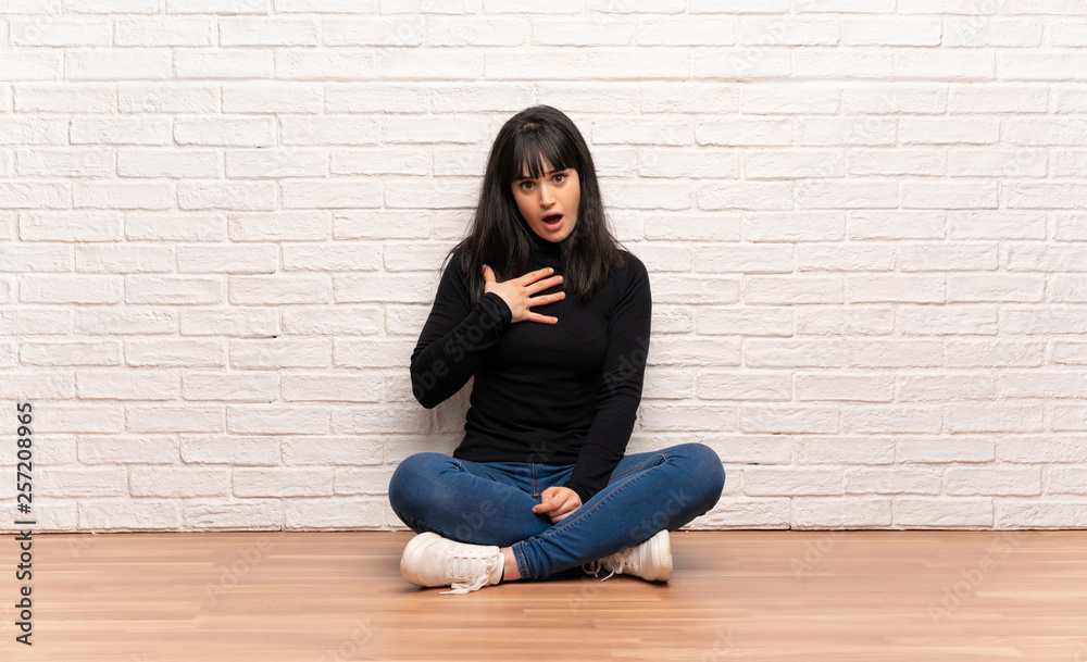 Woman sitting on the floor surprised and shocked while looking right Woman sitting on the floor surprised and shocked while looking right