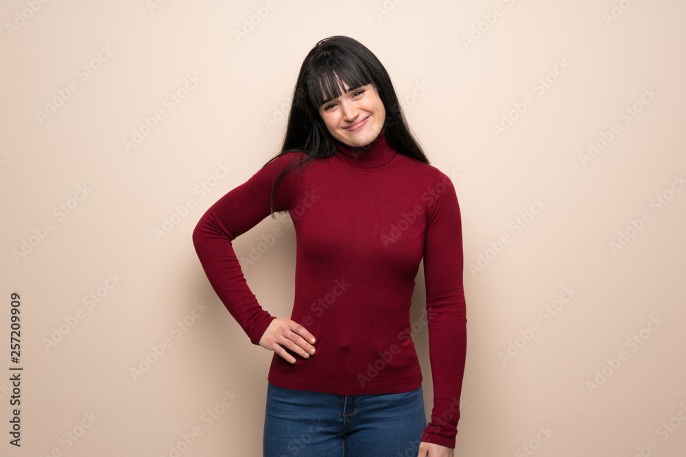 Young woman with red turtleneck posing with arms at hip and smiling Young woman with red turtleneck posing with arms at hip and smiling