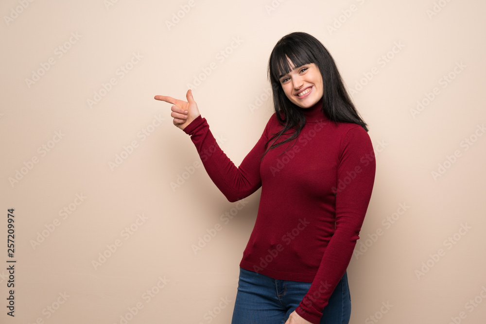 Young woman with red turtleneck pointing finger to the side in lateral position