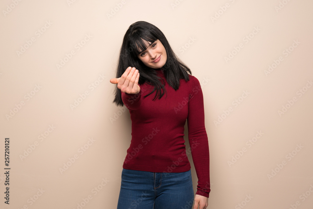 Young woman with red turtleneck inviting to come with hand. Happy that you came Young woman with red turtleneck inviting to come with hand. Happy that you came