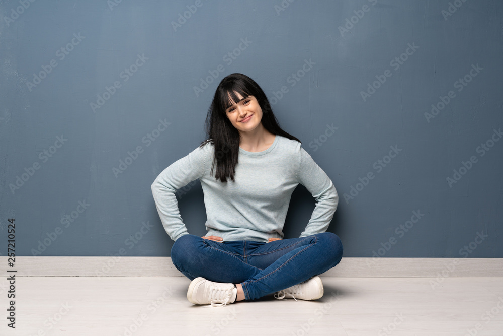 Woman sitting on the floor posing with arms at hip and smiling Woman sitting on the floor posing with arms at hip and smiling