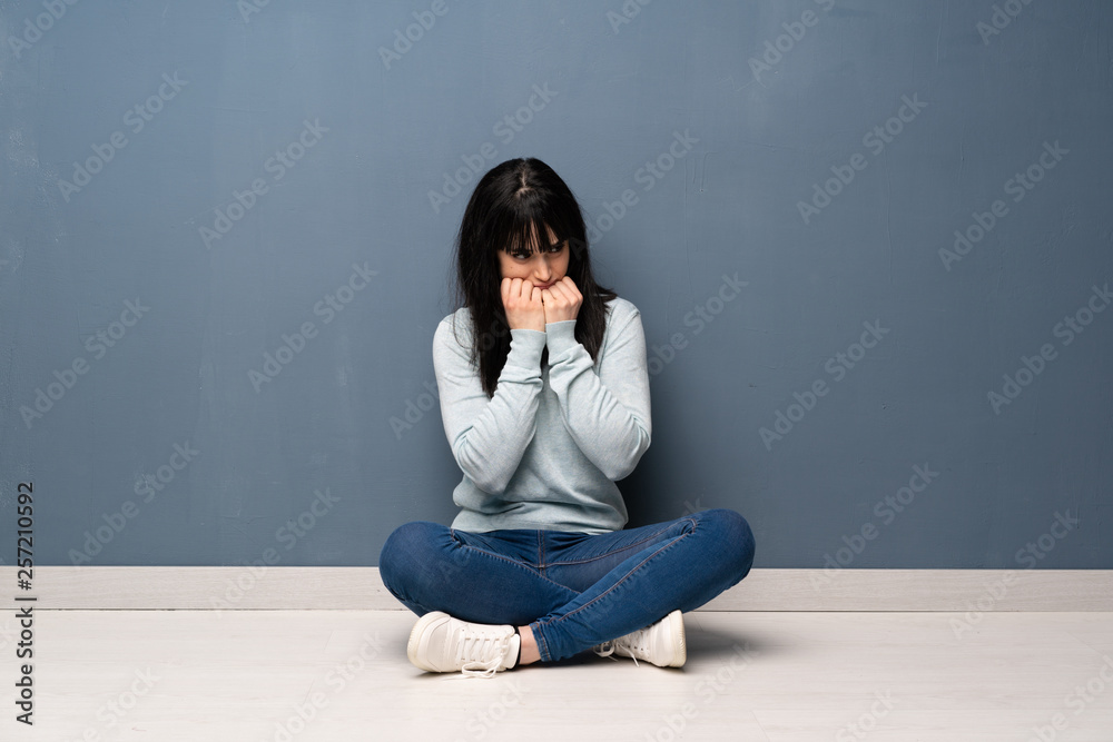 Woman sitting on the floor nervous and scared putting hands to mouth Woman sitting on the floor nervous and scared putting hands to mouth