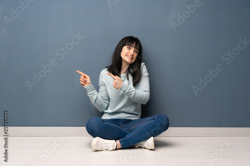 Woman sitting on the floor frightened and pointing to the side