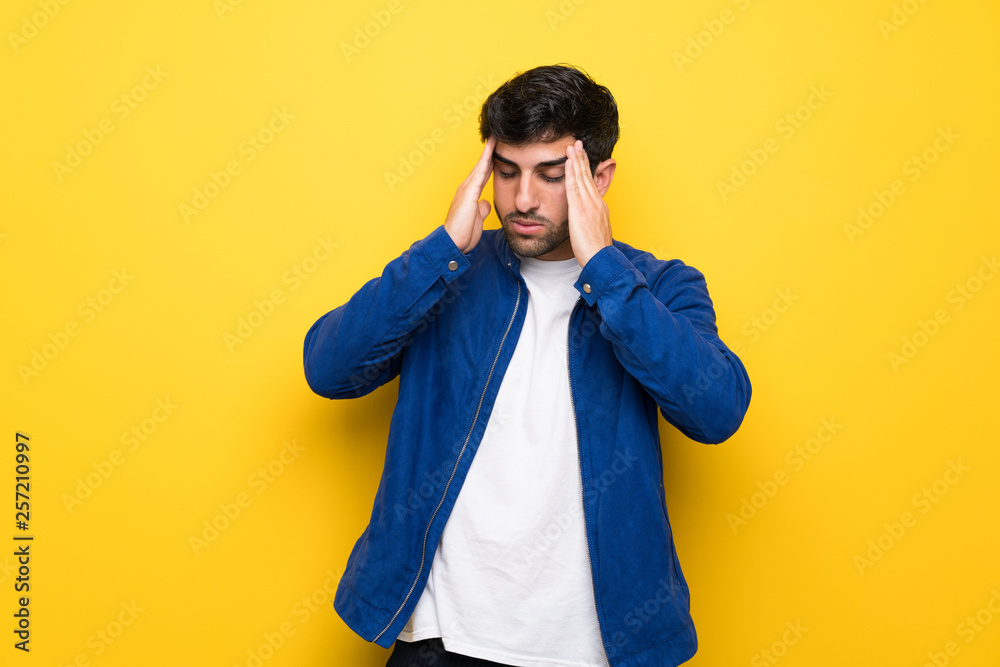 Man with blue jacket over yellow wall with headache Man with blue jacket over yellow wall with headache