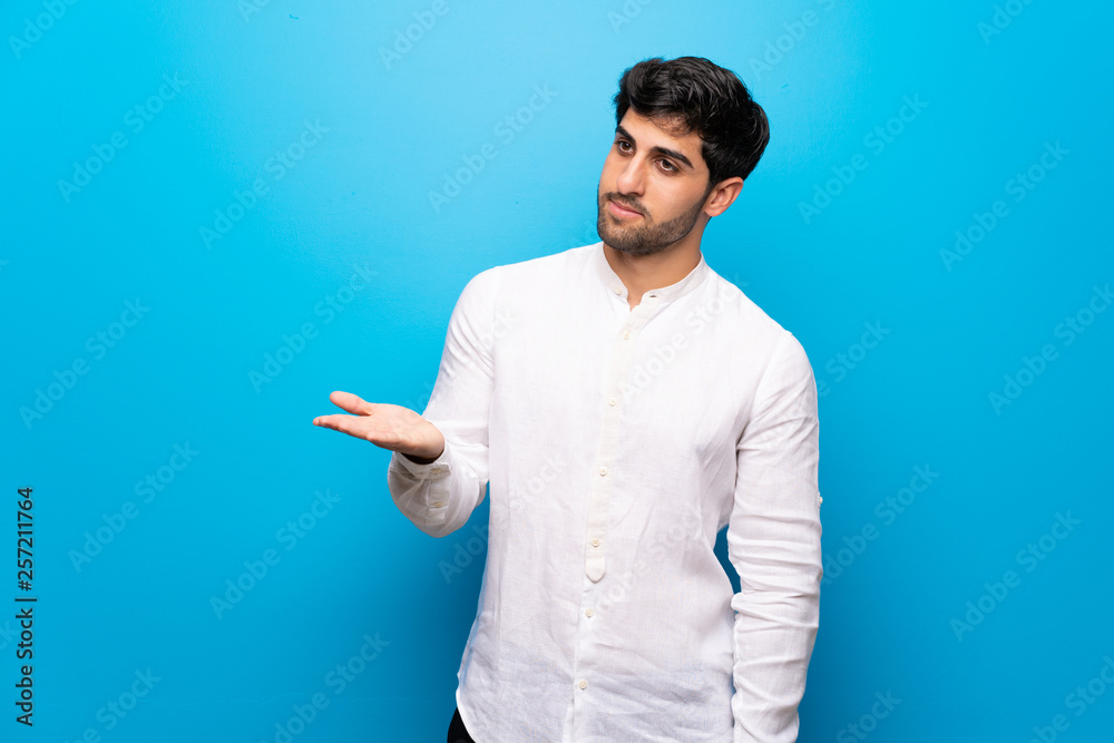 Young man over isolated blue wall presenting an idea while looking smiling towards