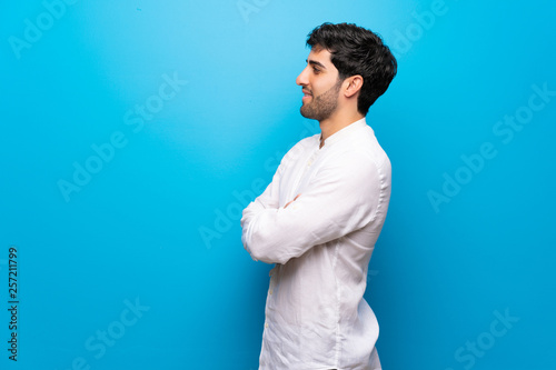 Young man over isolated blue wall in lateral position