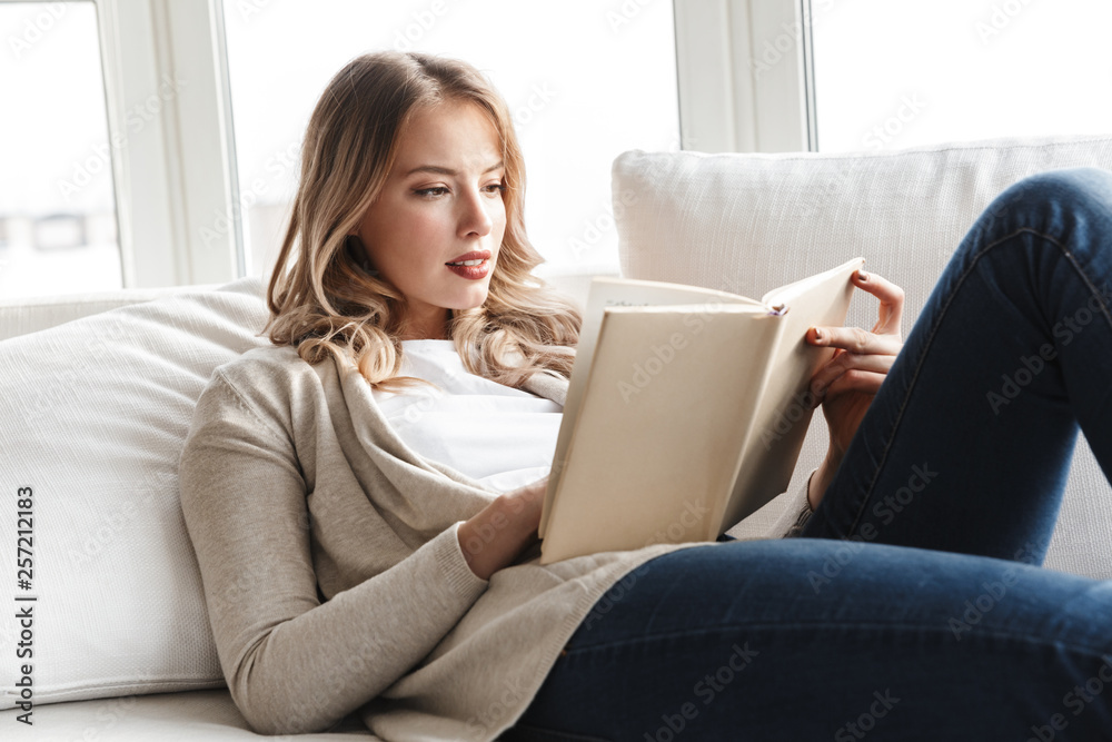 Blonde woman posing sitting indoors at home reading book. Blonde woman posing sitting indoors at home reading book.