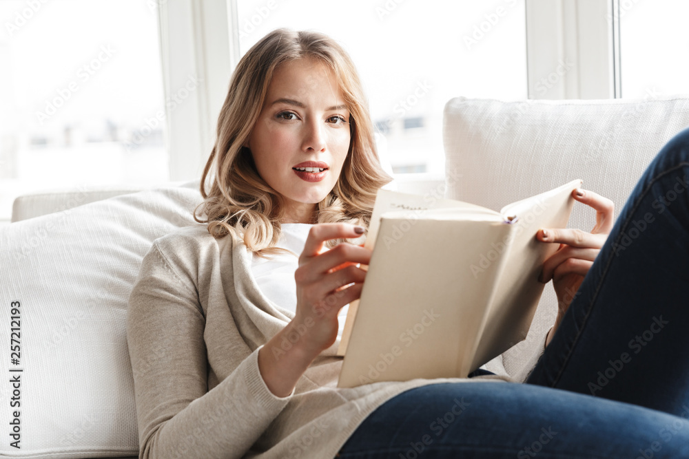 Blonde woman posing sitting indoors at home reading book. Blonde woman posing sitting indoors at home reading book.