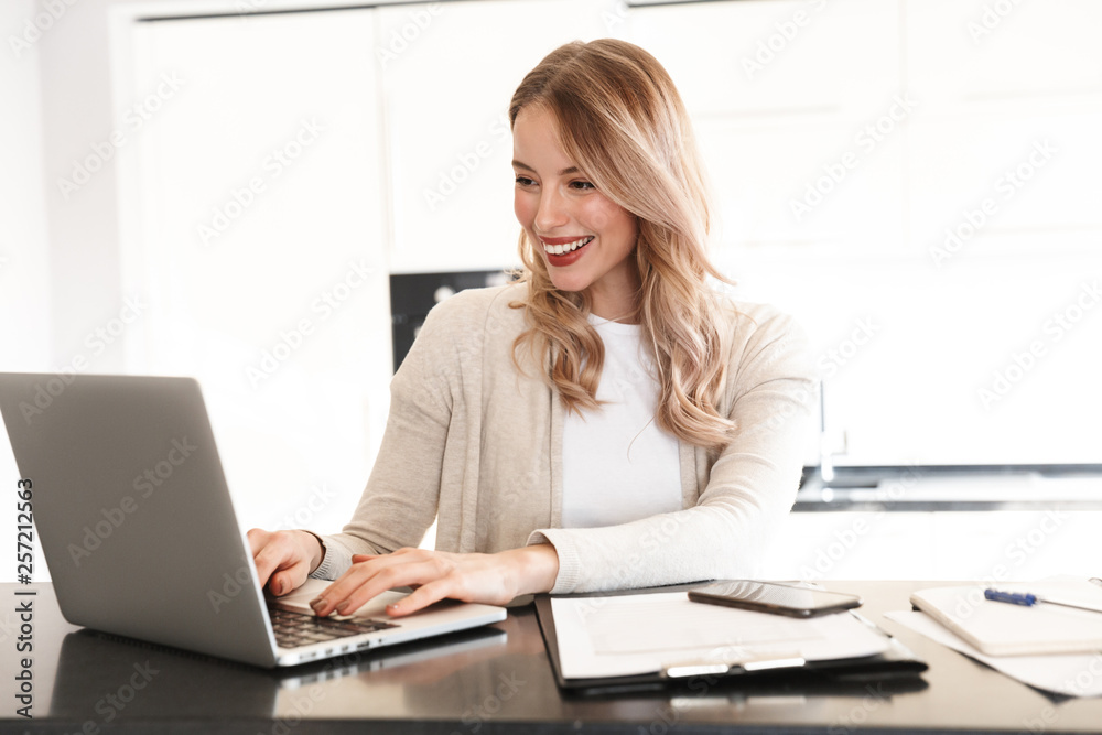 Beautiful blonde woman posing sitting indoors at home using laptop computer. Beautiful blonde woman posing sitting indoors at home using laptop computer.