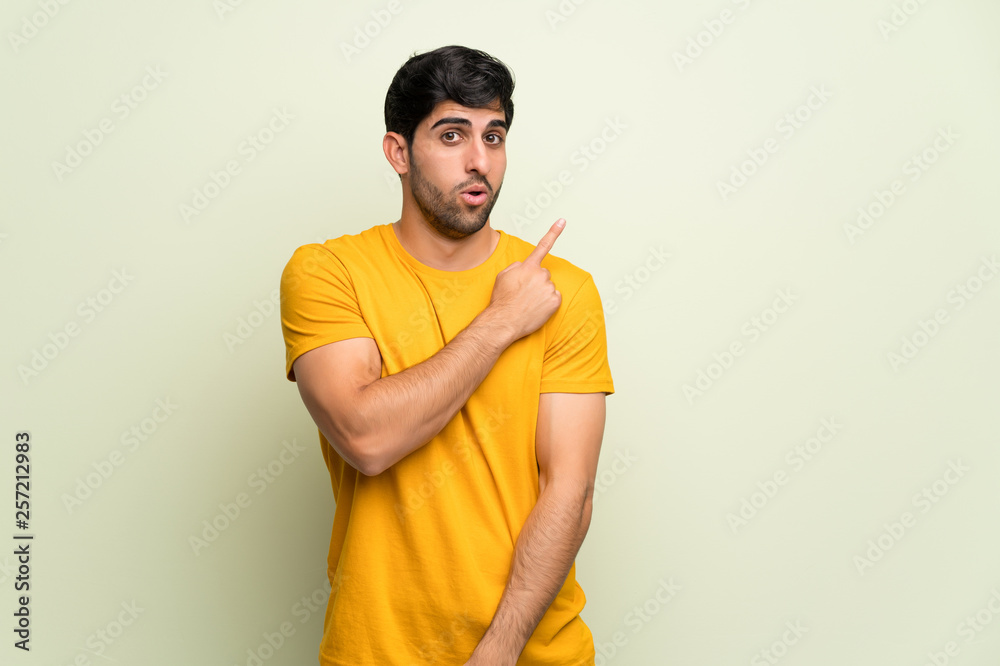 Young man over pink wall surprised and pointing side