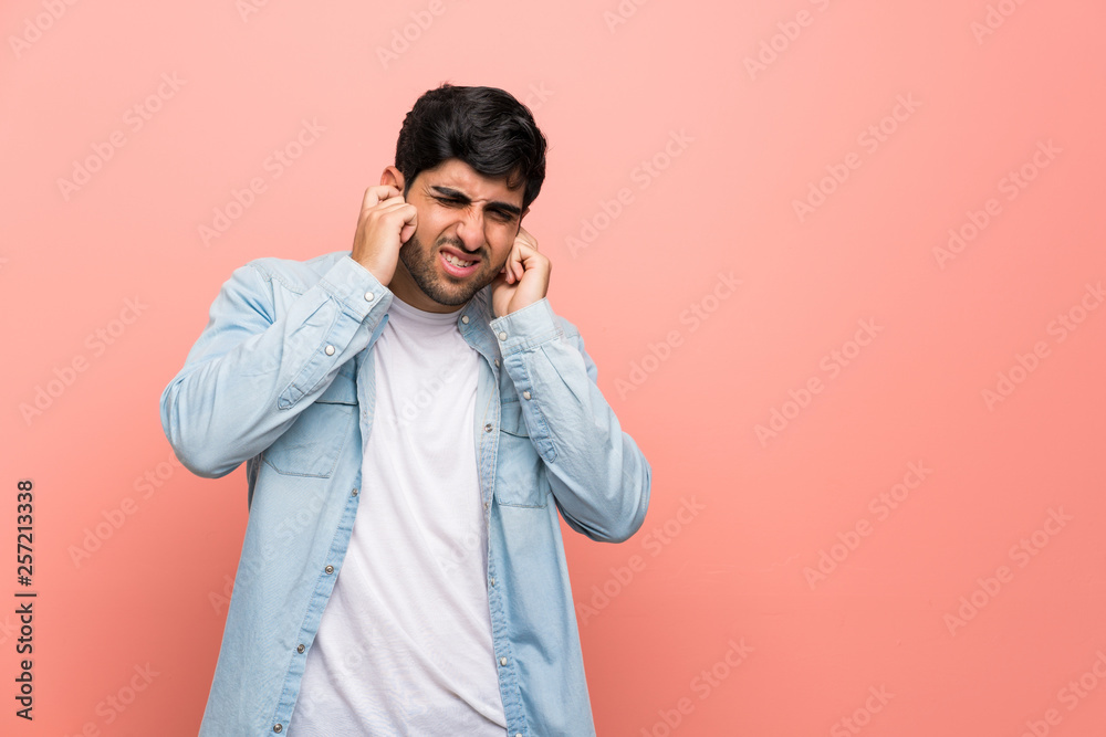 Young man over pink wall frustrated and covering ears Young man over pink wall frustrated and covering ears