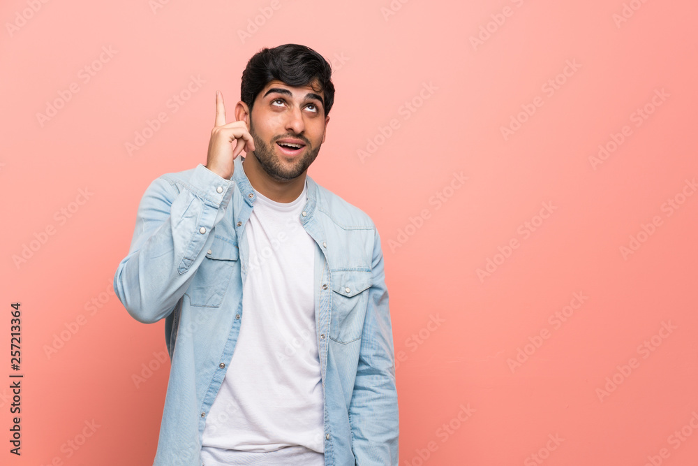 Young man over pink wall intending to realizes the solution while lifting a finger up Young man over pink wall intending to realizes the solution while lifting a finger up
